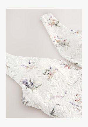 White floral-patterned top with textured surface and wide straps, featuring pastel colored flowers and a delicate leaf pattern.