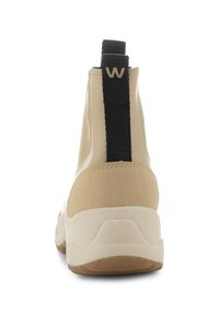 Zapatillas de caña baja color beige con un lazo elástico negro en el talón, parte superior texturizada y suela de amortiguación blanca. Materiales duraderos y diseño deportivo.