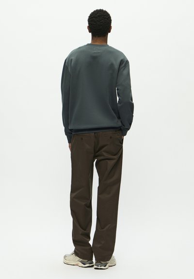 Sweatshirt à col rond de couleur gris foncé, associé à un pantalon marron. Les baskets présentent un design gris et noir. Texture lisse dans l'ensemble.