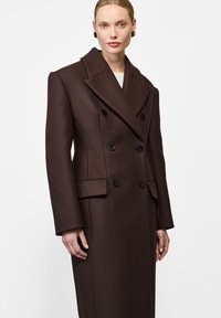 Brązowy płaszcz dwurzędowy z klapami, czarnymi guzikami i bocznymi kieszeniami. Wykonany z teksturowanej wełny, o dopasowanym kroju.