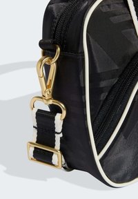 Czarna nylonowa torba ze złotymi okuciami, paskiem z tkaniny w paski oraz białym lamówką. Posiada zapinaną na suwak przegródkę oraz teksturowany materiał.