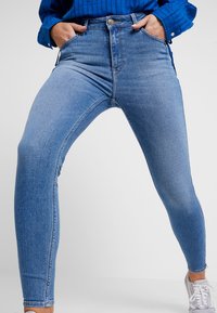 Vaqueros skinny de talle alto en azul, confeccionados en denim, con bolsillos traseros y cierre de botón, que presentan una textura limpia y suave.