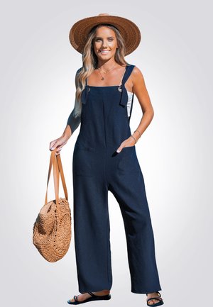 Salopette in lino blu navy con gambe larghe, spalline regolabili e tasche, abbinata a una borsa intrecciata e sandali flat.