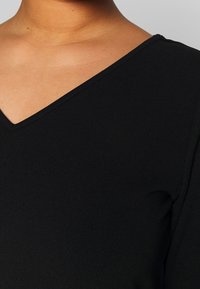 Schwarzes Oberteil mit V-Ausschnitt, glatter Textur und langen Ärmeln. Der Stoff ist leicht und etwas dehnbar.