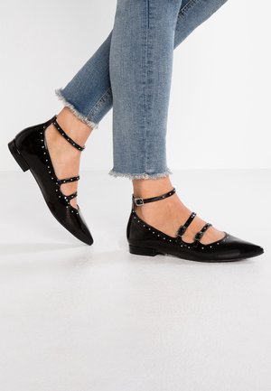 Czarne lakierowane baleriny z ostrymi noskami, wyposażone w trzy paski na kostkę ozdobione metalowymi ćwiekami. Noszone z jeansami z postrzępionymi nogawkami.