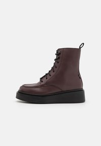 Botas de tornozelo em couro bordeaux com cordões pretos, apresentando uma biqueira arredondada e uma sola plataforma grossa preta para maior altura.