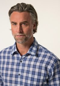 Camisa de cuadros azul y blanca con cuello puntiagudo, que presenta una sutil textura y botones negros. Primer plano de la camisa y el escote.