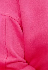 Fuchsia sweatshirtstof met een gladde textuur, met een zichtbare naad en een iets geplooid gedeelte, wat het speelse ontwerp benadrukt.