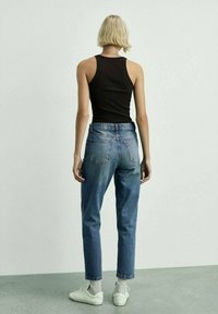 Črna rebrasta majica brez rokavov, modri hlače z visokim pasom, bele superge in siva nogavica. Hlače imajo zadnje žepe in ohlapen kroj.