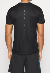Sort atletisk t-shirt med korte ærmer, der har vertikal aqua tekst "UNLIMITED PERFORMANCE" på ryggen og glat, fugttransporterende stof.