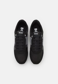 Černé tenisky s síťovaným svrškem a syntetickými detaily, s plochými tkaničkami a logem "BOSS" na jazyku a boku.