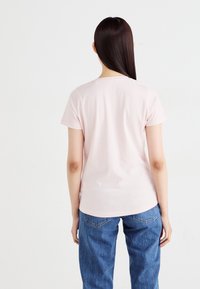 T-shirt de algodão rosa com gola redonda e mangas curtas, vista de costas. Usado com jeans de ganga azuis. Textura suave.