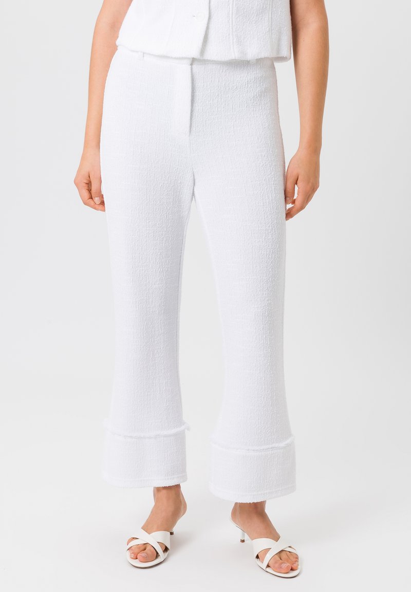 Witte textuurbroek met uitlopende pijpen en een zachte afwerking, met een vlakke voorkant en subtiele naaddetails. Gecombineerd met witte open-teddy-schoenen.