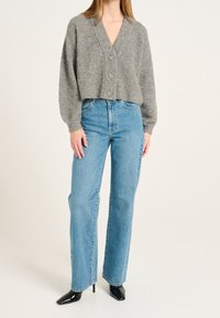 Grauer, cropped Pullover mit V-Ausschnitt und drei Knöpfen, kombiniert mit hellblauen, hoch geschnittenen, geraden Jeans und schwarzen, spitzen Pumps.