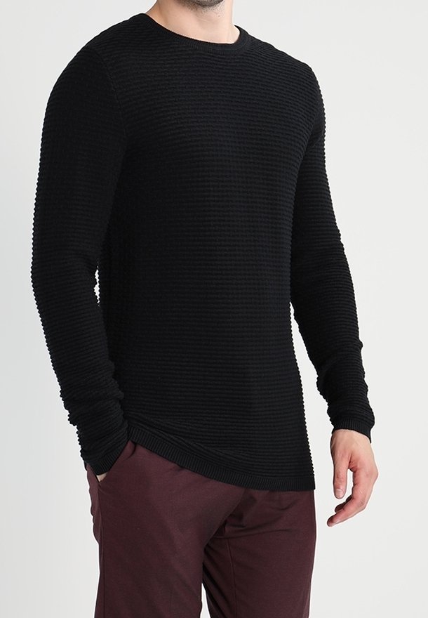 Pull noir à manches longues avec un design en côtes texturées, col rond et coupe ajustée, associé à un pantalon bordeaux.