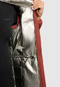 Padded coat with a metallic silver interior and a textured, rust-colored exterior. Features a drawstring and a smooth zipper.