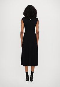 Vestido preto de malha canelada com corpete ajustado e saia evasé, design sem mangas, até à metade da panturrilha, combinado com botas pretas de salto.