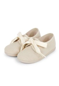 Beige canvas shoes with a textured surface, featuring a rounded toe, lace-up design with ribbon laces, and a flat flexible sole.