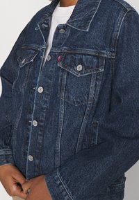 Mörkblå denimjacka med silverknappar, två bröstfickor och en klassisk krage. Tyget har en texturerad, något blekt look.