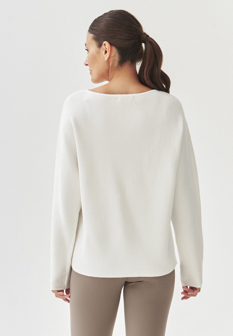 Biały, prążkowany sweter z szerokim dekoltem i ukośnymi detalami szycia. Połączony z dopasowanymi brązowymi spodniami. Ogólnie luźny krój.