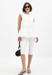 Valge ilma varrukateta tunika kihilise disainiga, koos valgete kapri pükstega. Aksessuaarideks on väike must ümmargune käekott ja mustad sandaalid.