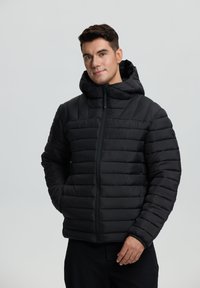 Sort pufferjakke med en struktureret, quiltet design, der har en tætsiddende hætte og lynlås. Blødt, isoleret materiale til varme.