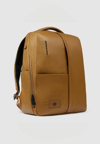 Bruine leren laptoprugzak met een gestructureerde vorm, een voorvak met rits, verstelbare riemen en een merkdetail aan de zijkant.