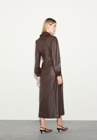 Brun læder midi-kjole med krave, lange ærmer og puffede manchetter, med en glat tekstur. Stylet med sorte og brune mønstrede hæle.