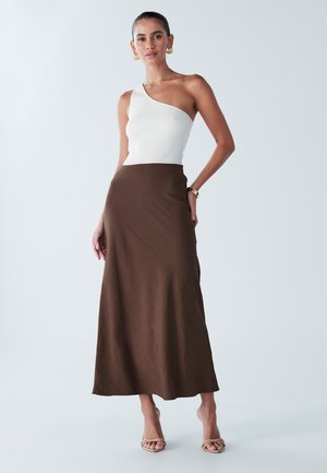 White ribbed one-shoulder top paired with a flowing brown maxi skirt. Features smooth texture and a relaxed silhouette. Simple strappy sandals.