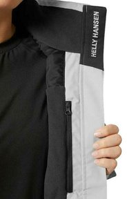 Helly Hansen jacket featuring a light gray exterior, black fleece lining, zippered pocket, and embroidered logo on the collar.