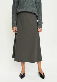 Pull gris avec tricot texturé associé à une jupe midi à motifs sombres. Des chaussures noires à bout pointu complètent la tenue.