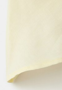 Blødt gult stof med en ren kant, der viser tekstur og let fald mod en hvid baggrund.