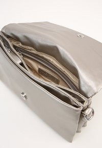 Metalická stříbrná kabelka s hladkým koženým povrchem. Disponuje bezpečným zapínáním na cvok a několika vnitřními přihrádkami pro lepší organizaci.