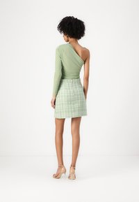 Groene top met één schouder, gecombineerd met een mintgroene tweed minirok. De top heeft een slim fit ontwerp en de rok heeft een ritssluiting en een gestructureerd patroon.