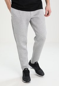 Grå sweatpants med en slät yta, avsmalnande bendesign och framträdande sömdetaljer; bärs med svarta träningsskor.
