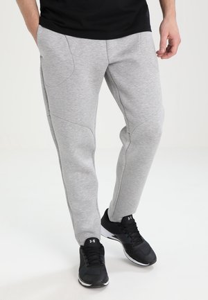 Graue Jogginghosen mit glatter Textur, eng zulaufendem Bein und ausgeprägten Nahtdetails; getragen mit schwarzen Sportschuhen.