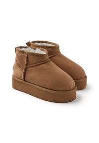 Botas de tobillo de ante sintético marrón con un acabado texturizado, forro blanco suave, punta redondeada y suela de plataforma baja. Presenta un tirador en la parte posterior.
