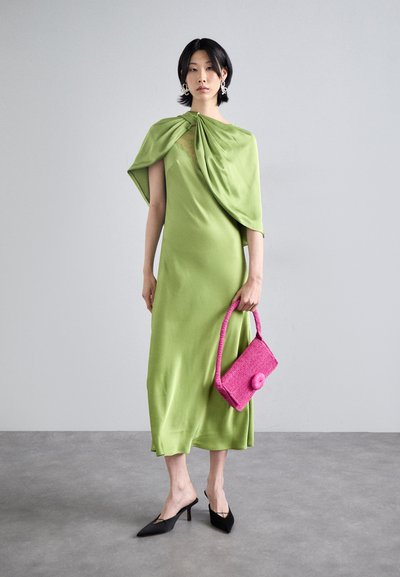 Abito in satin verde con spalla drappeggiata asimmetrica, abbinato a una borsa rosa texturizzata e tacchi neri a punta. Tessuto morbido e scorrevole.