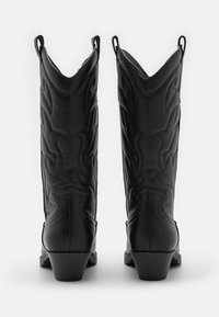 Botas de cowboy de cuero negro con un acabado texturizado, que presentan una punta afilada, un caña alta y un patrón de costura decorativa. Tacón bajo.
