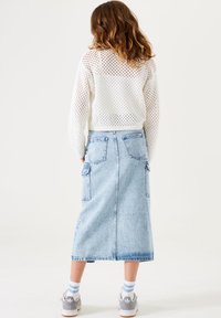 Pull en tricot blanc perforé ; jupe en denim bleu clair mi-longue avec poches ; baskets grises avec accents blancs et chaussettes rayées bleues.