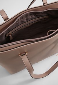 Jasnoróżowa skórzana torba typu tote z podwójnymi uchwytami, wyposażona w kieszeń na zamek błyskawiczny i gładkie wyściółki wnętrza, z delikatnym detalem logo.