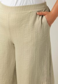 Lichtbeige wijde broek van textuurstof met subtiele verticale strepen, met zijkanten zakken en een relaxte pasvorm.