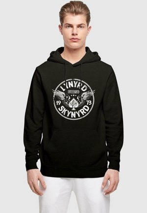 Black hoodie featuring a circular graphic with "Lynyrd Skynyrd Freebird" text, eagle accents, and a year. Soft texture, kangaroo pocket.