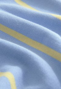 Tejido de color azul claro con un tejido texturizado, que presenta franjas horizontales en amarillo. La superficie parece suave con una sutil profundidad y relieve.