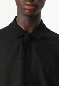 Camisa polo preta com um tecido texturizado, apresentando um colarinho clássico, placket de meia-abotoadura e um detalhe de logótipo subtil no peito.