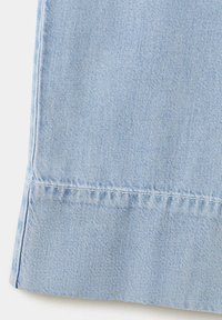 Tissu en denim bleu clair avec coutures visibles, montrant la texture et les détails du tissage.