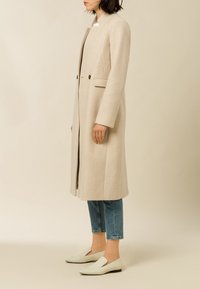 Beige wollen blend jas met een rechte snit, twee voorkruiden en een minimalistisch ontwerp. Gecombineerd met cropped blauwe jeans en witte instappers.