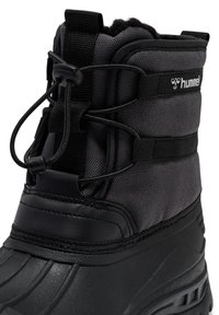 Czarne śniegowce z teksturowanym wierzchem, wyposażone w elastyczne sznurowadła, wyściełany kołnierz oraz trwałą gumową podeszwę. Logo marki widoczne z boku.