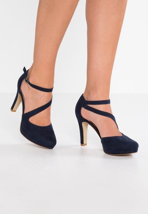 Granatowe zamszowe szpilki na platformie, z krzyżującymi się paskami i klamrą przy kostce, podkreślone złotym detalem na obcasie.