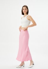 Gonna lunga e fluida di colore rosa con una consistenza liscia, vita elastica, abbinata a un top corto a costine bianco e scarpe con tacco bianche.